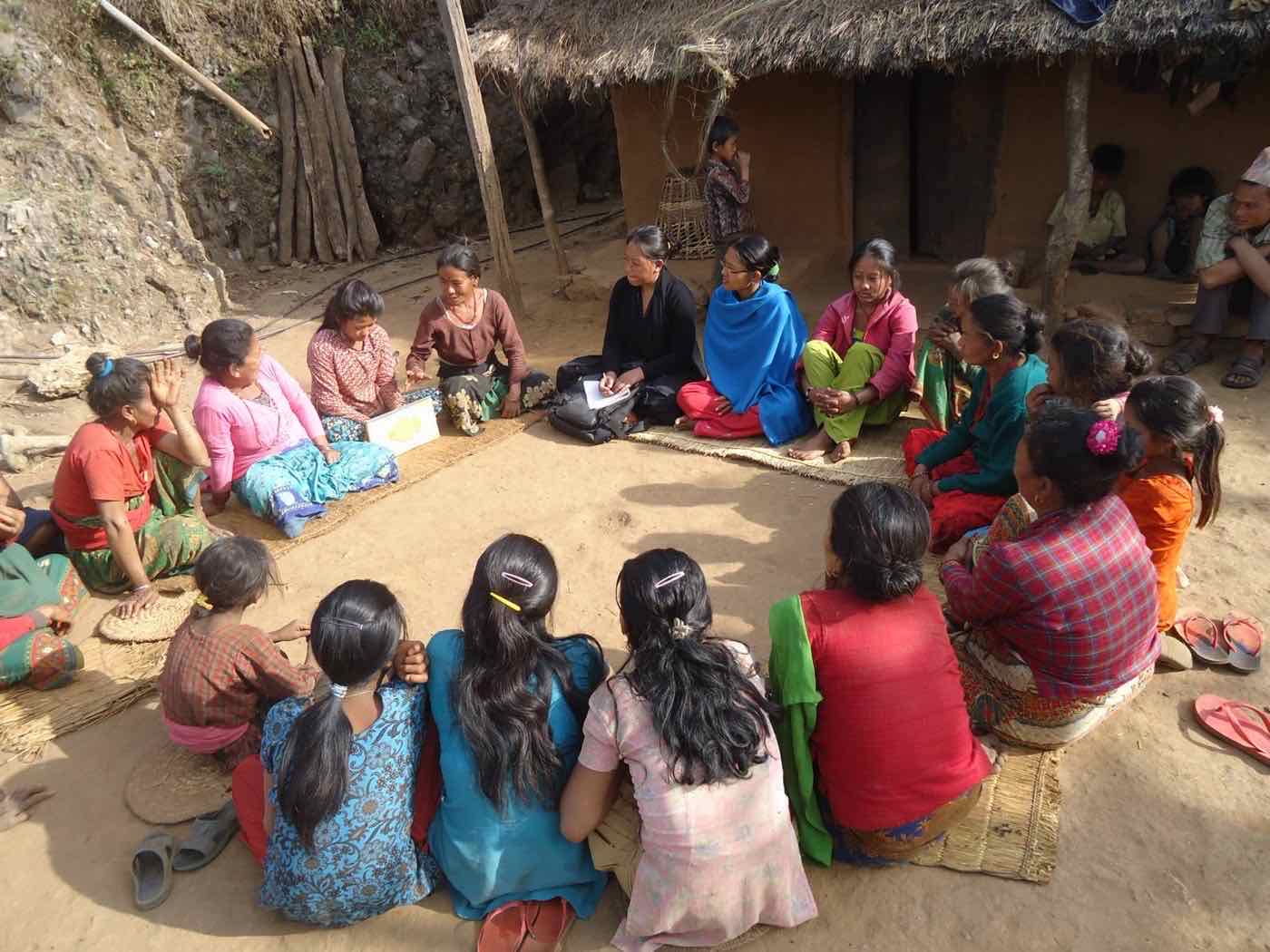A women's group meeting in a circle outside a thatched house
