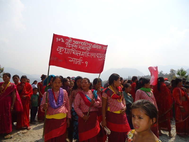 A women's group marching with a red banner on International Women's Day