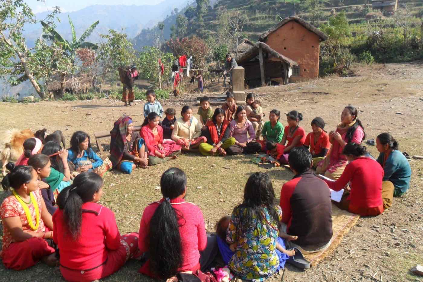 Women and children gathered in a large circle on a hillside above a mountain valley