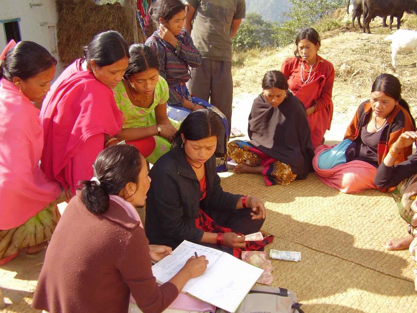 Women of an AWEP group counting cash and recording deposits in a ledger during a savings meeting