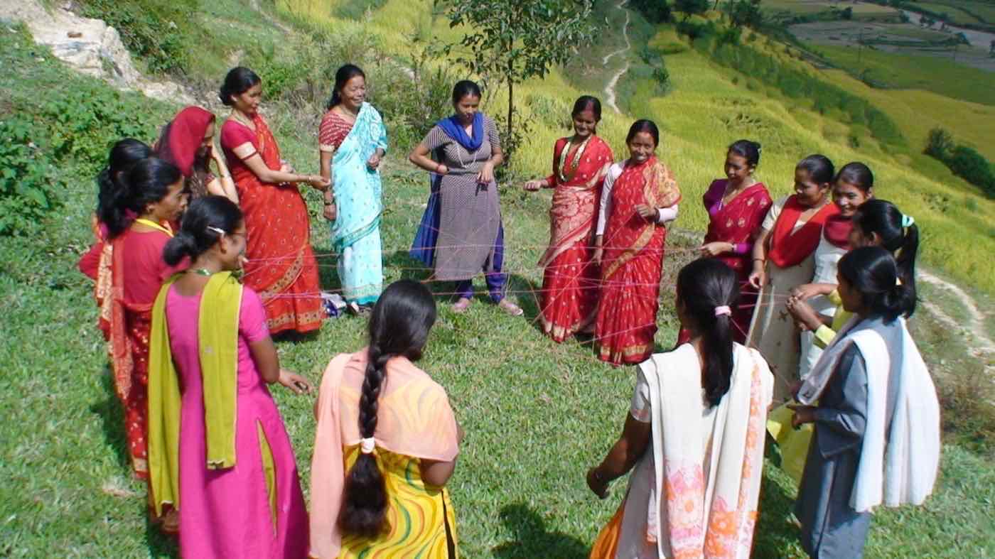 Women standing in a circle on a terraced hillside, holding a web of string in a group activity