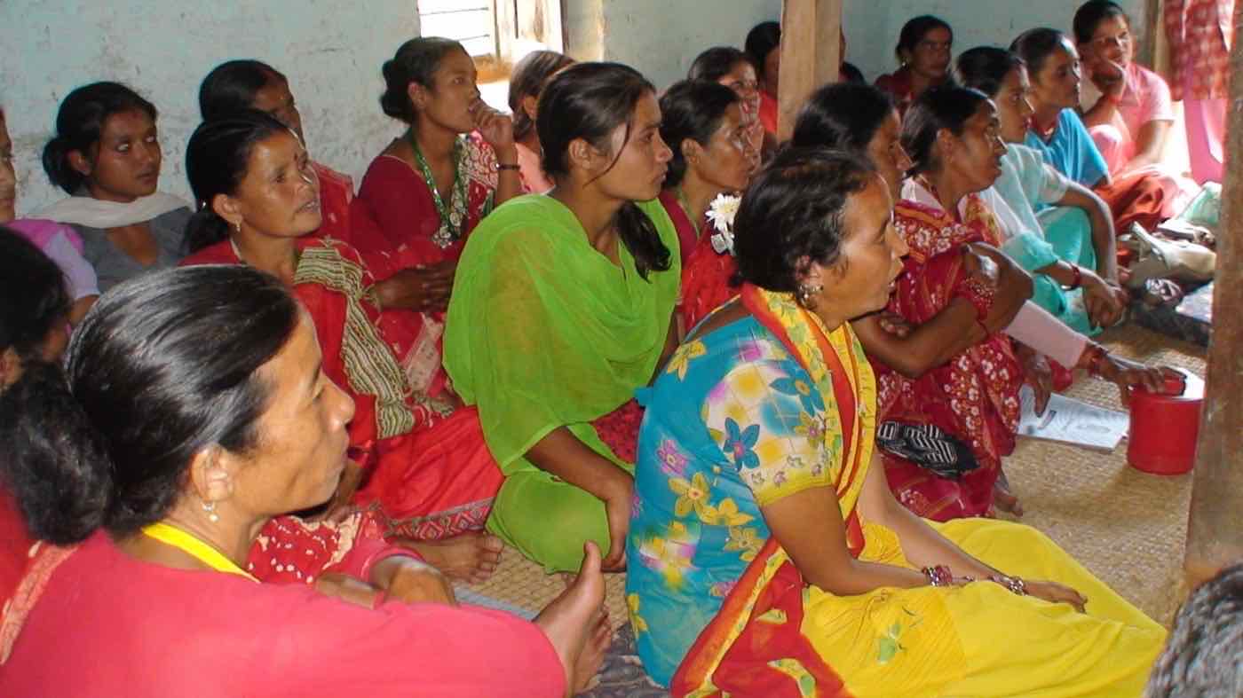 Women seated on a mat, listening during a community group meeting