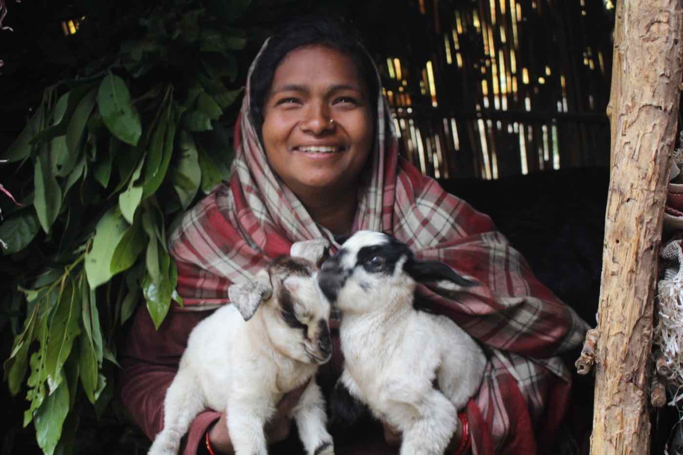 A woman smiling with two young goats she is raising through the Dignity Project