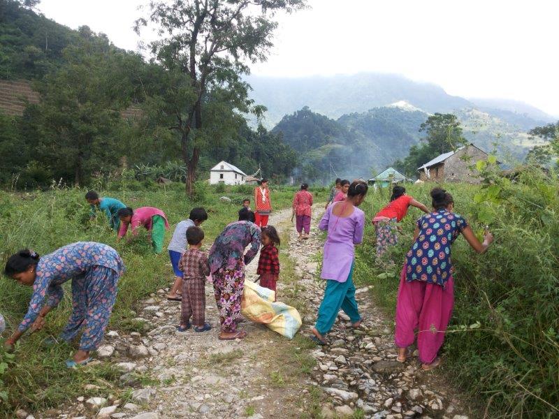 Women and children clearing a village path together during a community clean-up