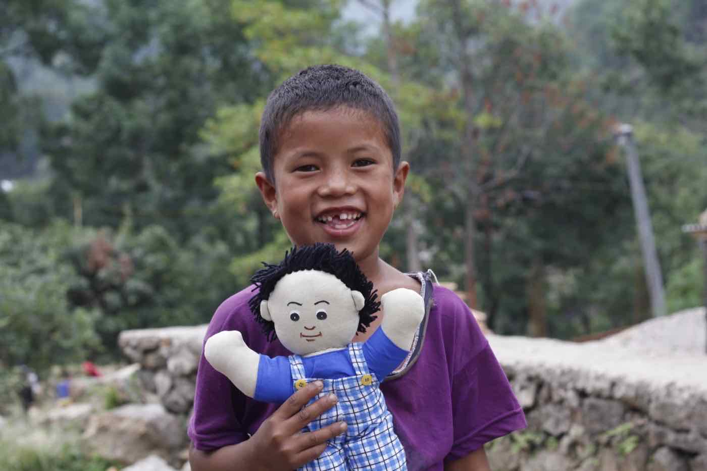 A boy smiling as he holds a child learning material doll received by child group members in the Harmony Project