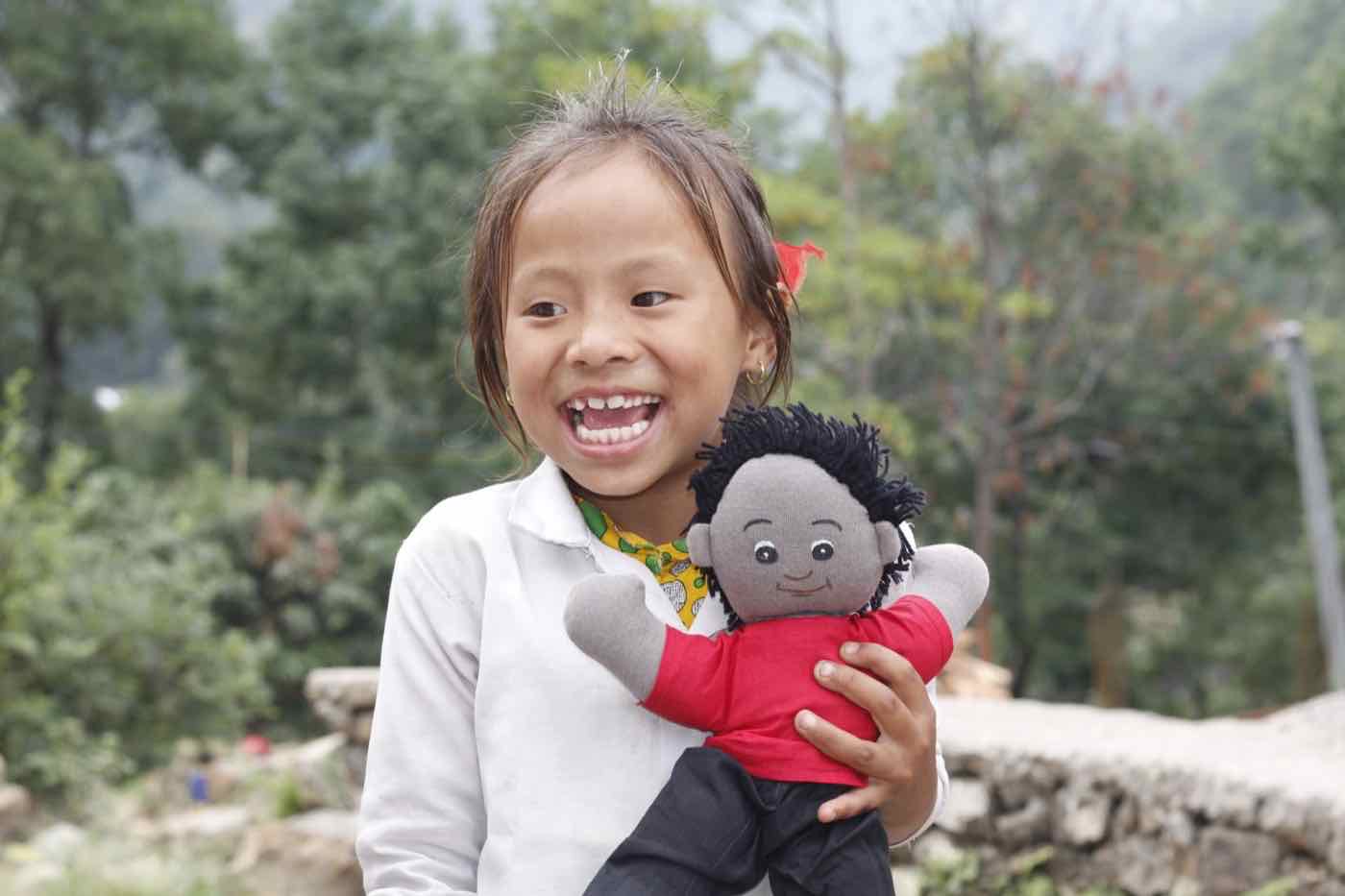 A girl laughing while holding a child learning material doll received by child group members in the Harmony Project
