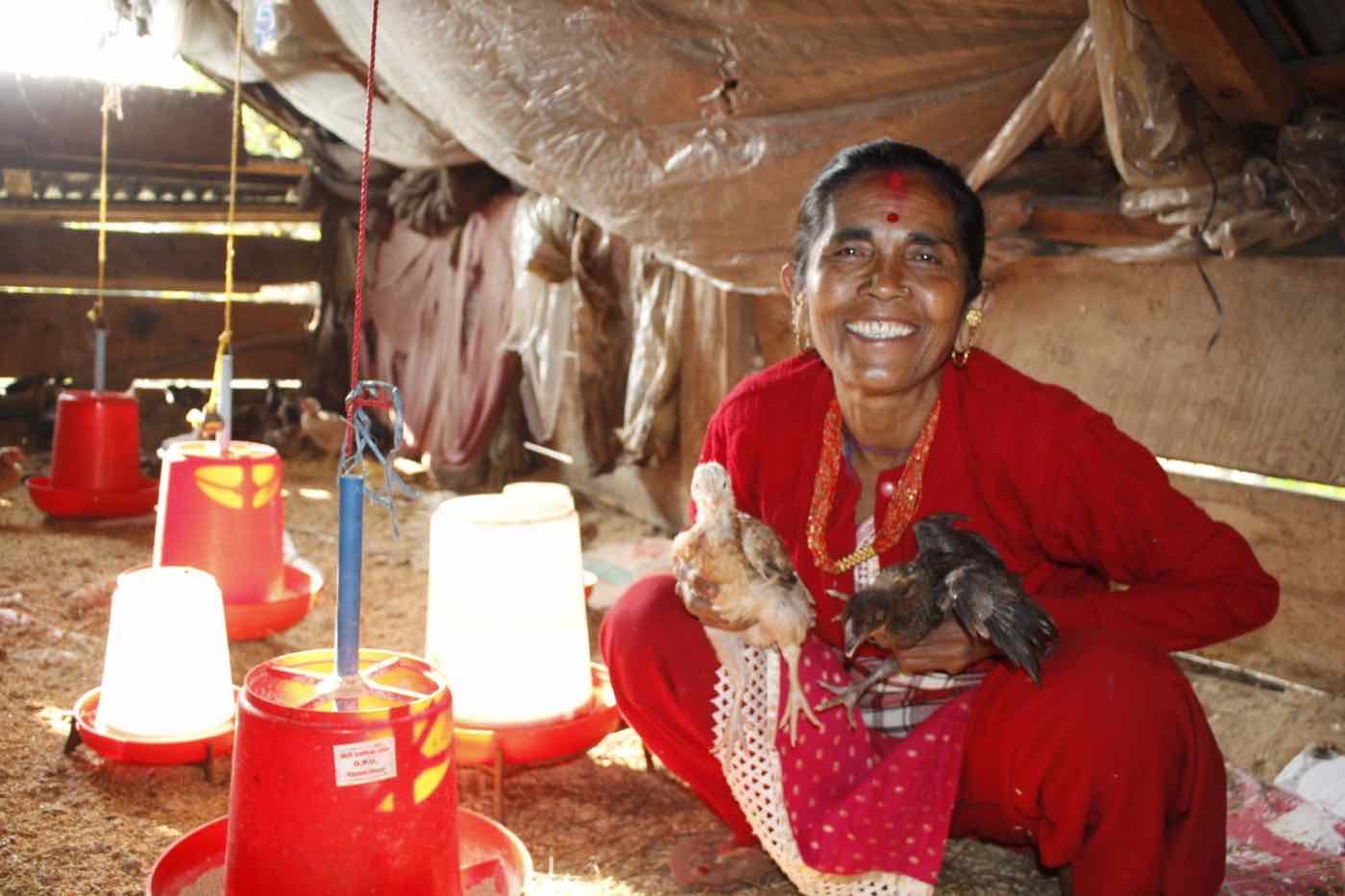 A smiling woman holding two young chickens inside her coop, raised through the Hope Project