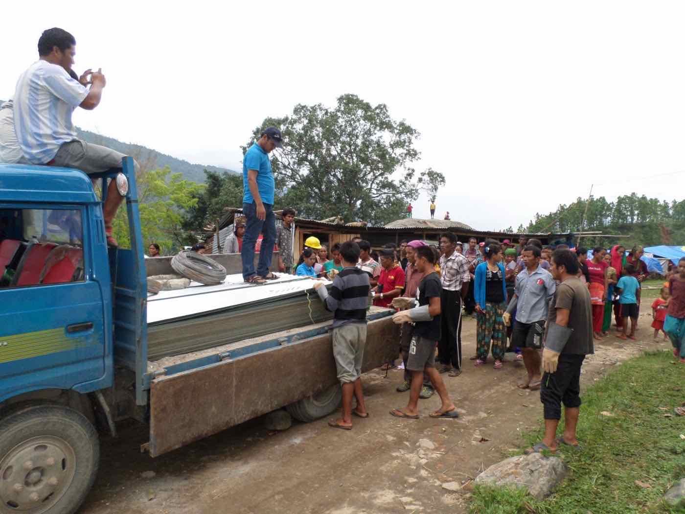 Villagers collecting CGI roofing sheets and wire from a truck for HARP emergency shelters