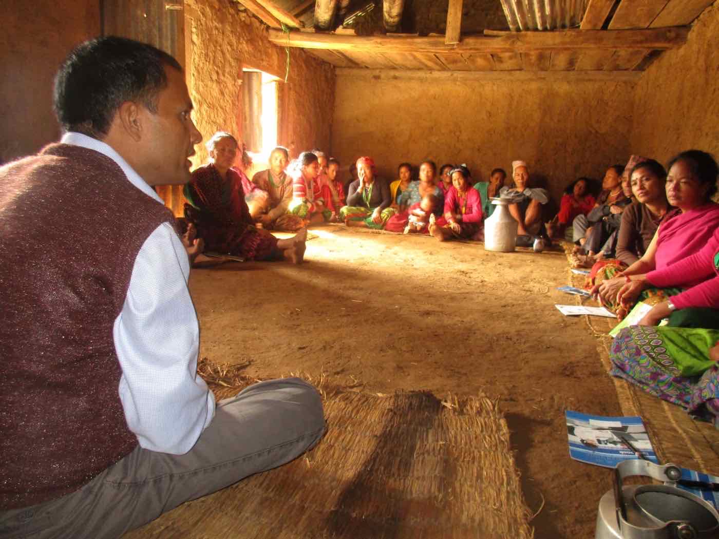 Villagers gathered inside a mud-walled home for a HARP poultry training in Talakhu