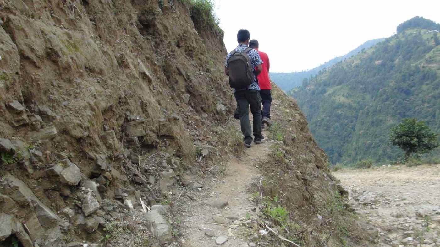 Joy Project staff walking a narrow mountain trail to reach remote households in Nuwakot