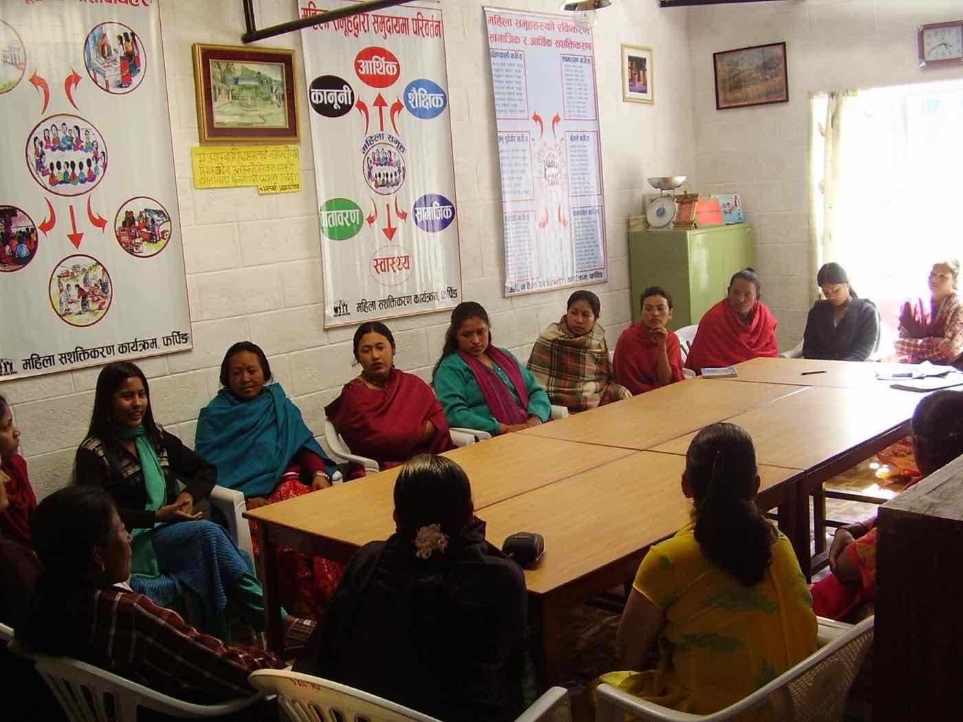 A women's group meeting around a table beneath Women Empowerment Program posters
