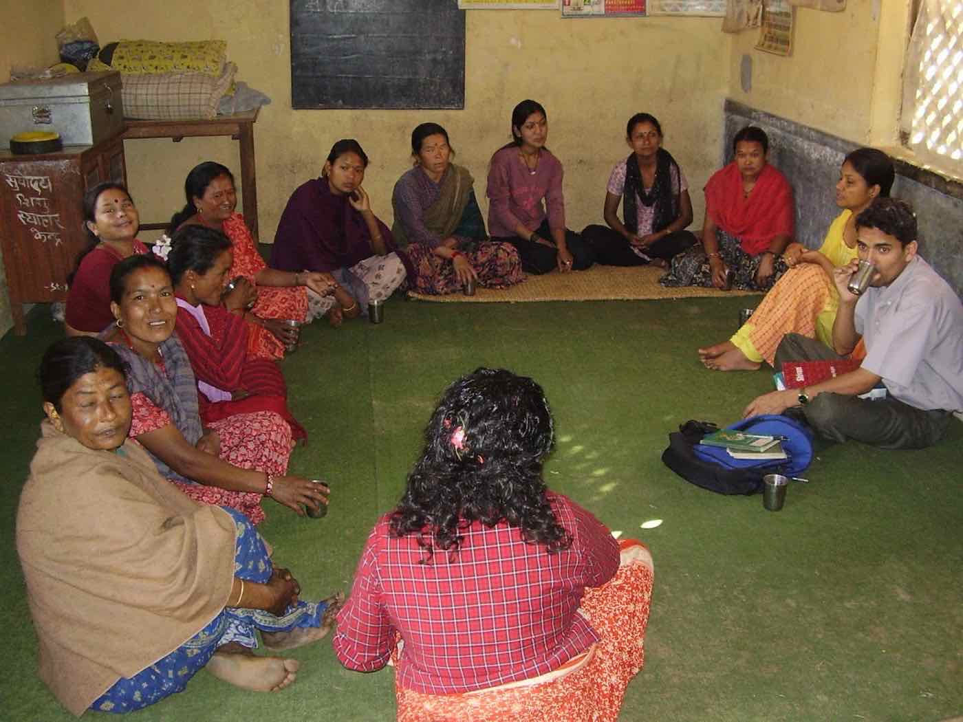 Women sitting in a circle on a green mat, sharing tea during a group discussion