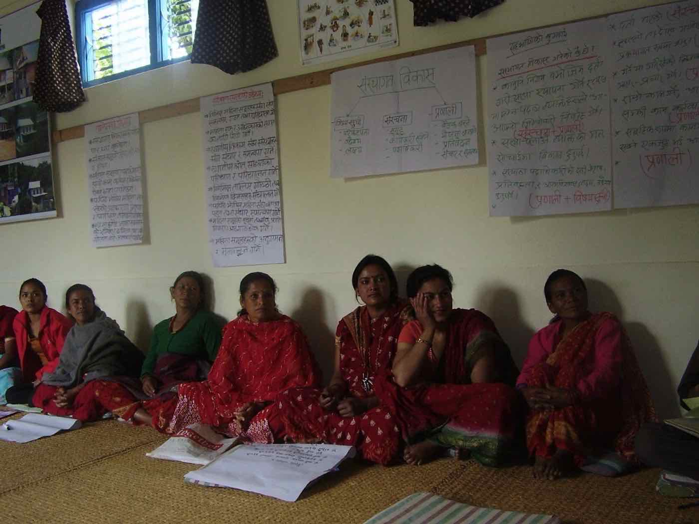 Women seated in a row against a wall covered in hand-written training charts