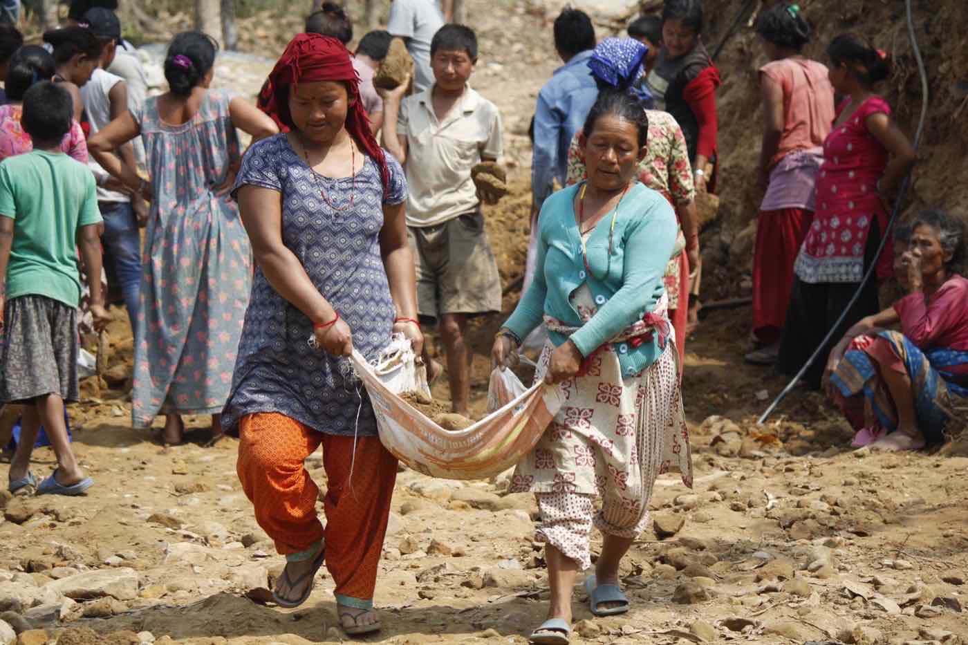 Two women carrying soil together in a cloth sling during community construction work