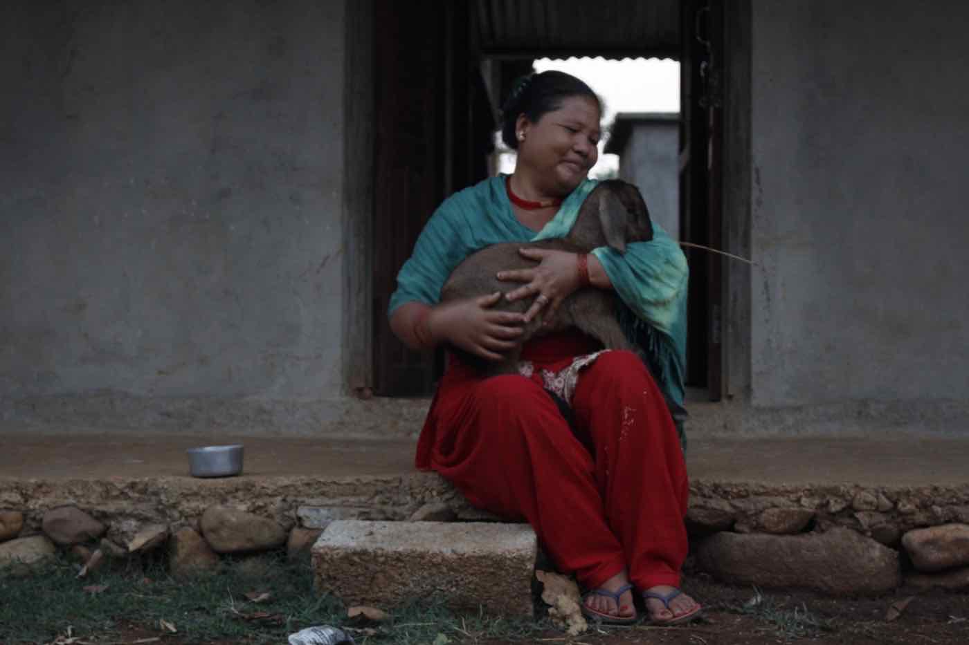 A smiling woman holding a young goat on her doorstep