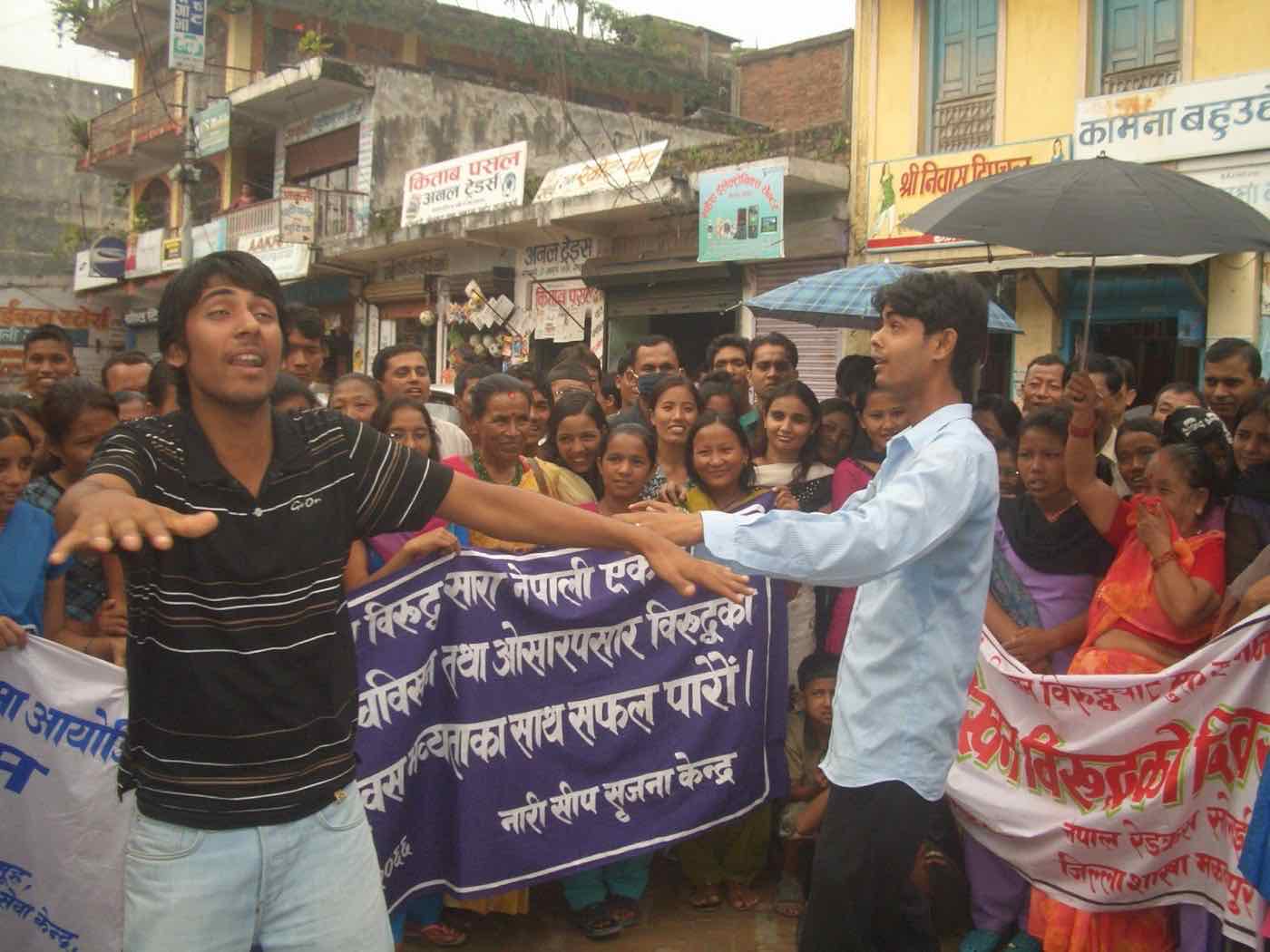 Young men performing an anti-trafficking street drama before a crowd holding banners