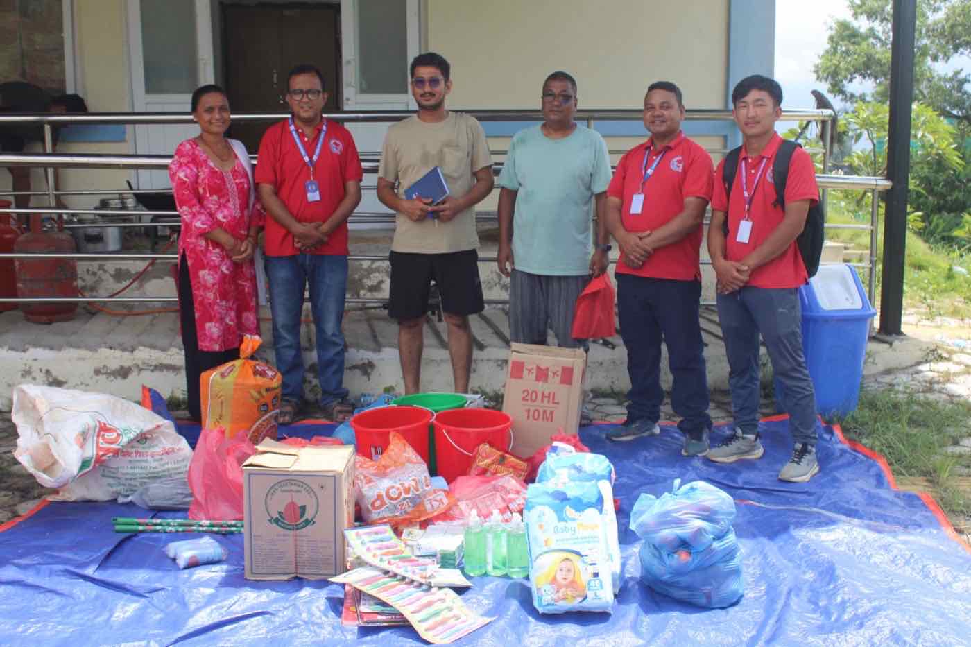 Share and Care Nepal staff beside relief supplies laid out for distribution, including rice, lentils, buckets, soap and other household items