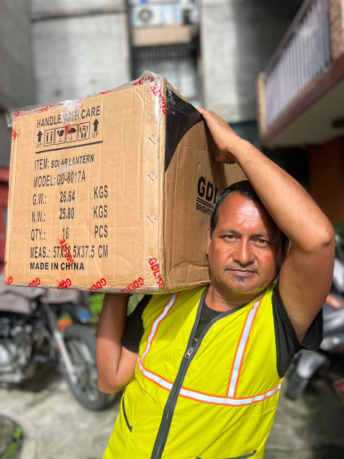 A staff member carrying a case of solar lanterns on his shoulder as relief supplies are loaded