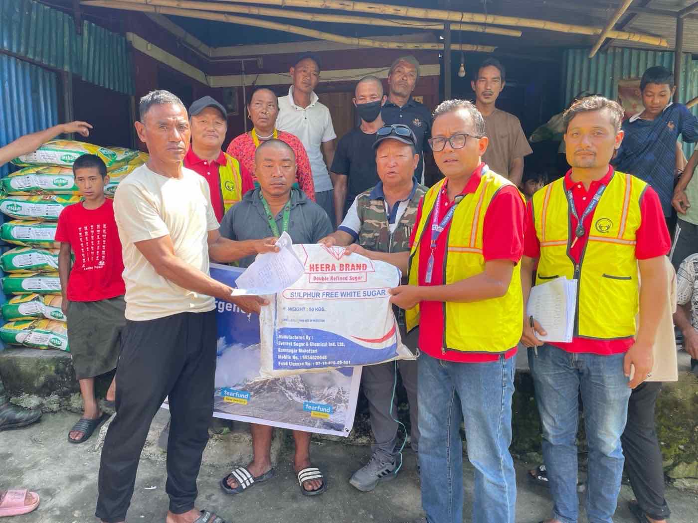Share and Care Nepal staff handing a 50kg sack of sugar to a resident, in front of a RISE banner carrying the Tearfund New Zealand and Tearfund Australia logos