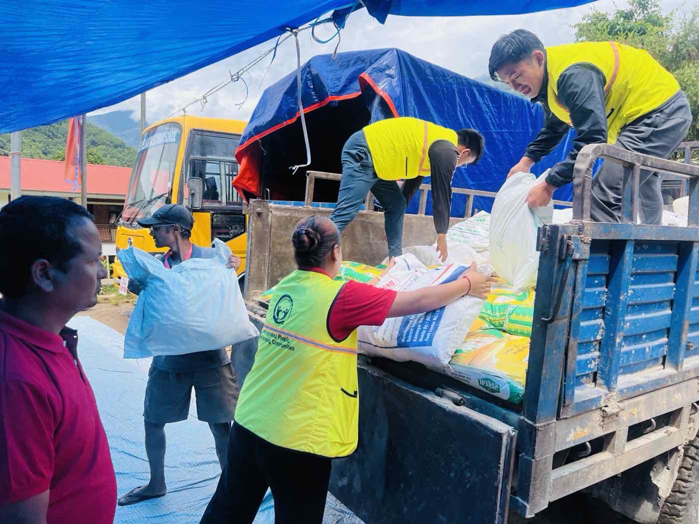 Staff in high visibility vests unloading sacks of rice and sugar from a truck at a RISE distribution point