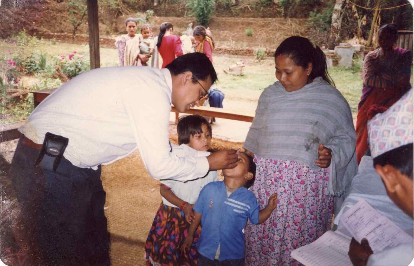 A CBHDP health worker giving a child oral medicine on a village porch